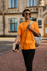 Young man with headphones and backpack walking by college outdoors
