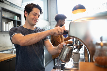 Smiling barista steaming milk at cafe