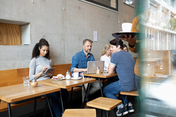 Customers using wireless gadgets sitting at table in coffee shop