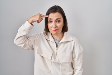 Middle age hispanic woman standing over isolated background pointing unhappy to pimple on forehead, ugly infection of blackhead. acne and skin problem