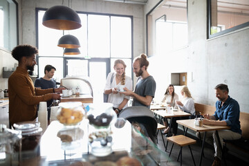 Barista at counter giving coffee to smiling customers