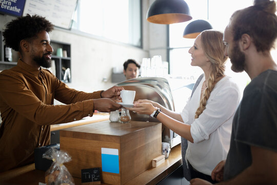 Smiling barista serving coffee to couple in cafe