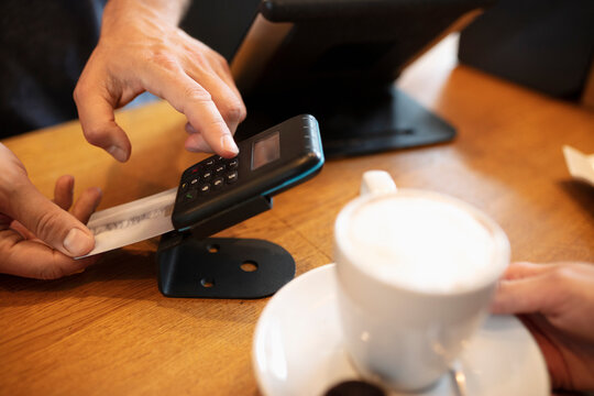 Hands of cashier using card machine at cafe counter