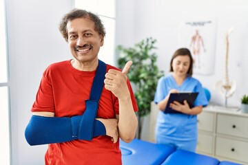 Southeast asian man wearing wearing arm on sling at rehabilitation clinic smiling happy and...
