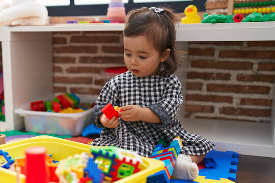 Adorable chinese girl playing with construction blocks sitting on floor at kindergarten
