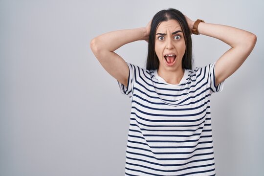 Young brunette woman wearing striped t shirt crazy and scared with hands on head, afraid and surprised of shock with open mouth