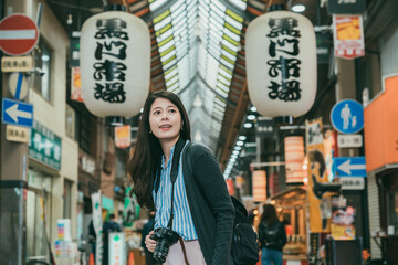 pretty Taiwanese girl with camera enjoying the view at the exit of kuromon ichiba market in Osaka...