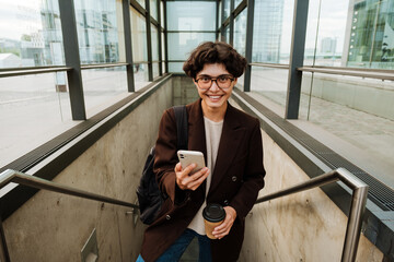 European woman using cellphone and drinking coffee at underpass