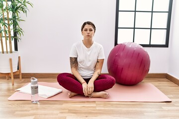 Young hispanic woman training at sport center puffing cheeks with funny face. mouth inflated with...