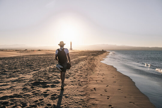 Man Walking Near Shore On Beach At Sunset