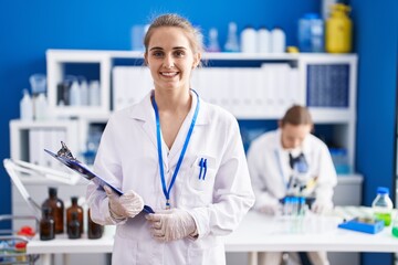 Blonde woman working at scientist laboratory looking positive and happy standing and smiling with a confident smile showing teeth