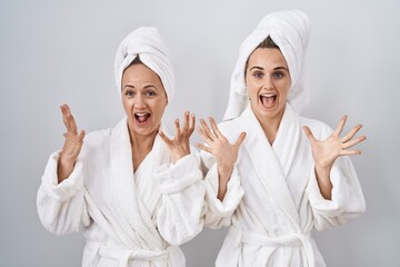 Middle age woman and daughter wearing white bathrobe and towel celebrating crazy and amazed for...