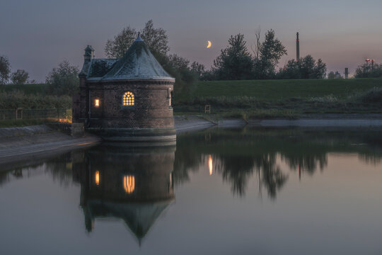 Germany, Hamburg, Historic filter house on Kaltehofe island reflecting in Elbe river at dusk