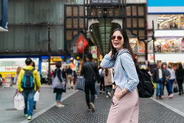 happy fashionable Asian female tourist wearing sunglasses turning to smile at camera near shinsaibashisuji station shopping district in Osaka japan