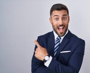 Handsome hispanic man wearing suit and tie with a big smile on face, pointing with hand finger to...