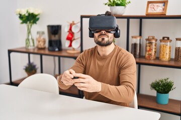 Young hispanic man playing video game using virtual reality glasses at home
