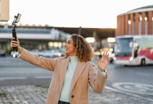 Smiling woman gesturing and recording video through mobile phone on tripod