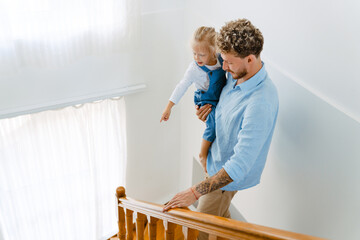 Young white father going down on stairs with little daughter at home