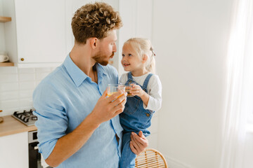 Young white father holding his little daughter while drinking juice together