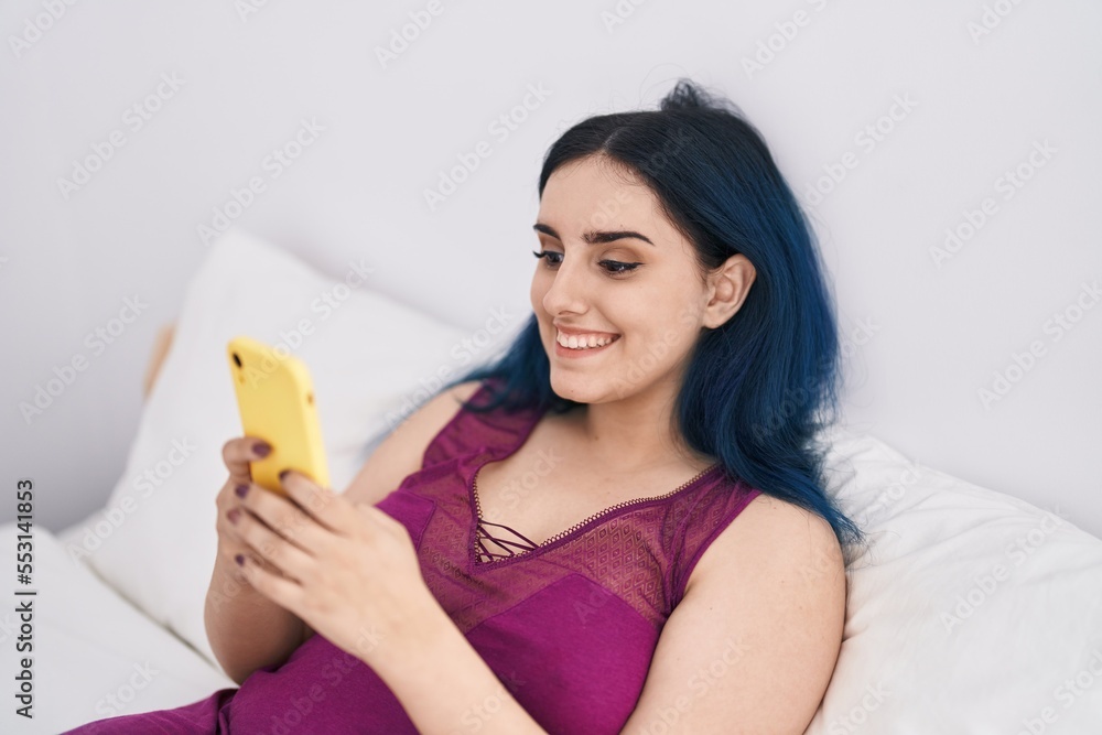 Poster Young caucasian woman using smartphone sitting on bed at bedroom