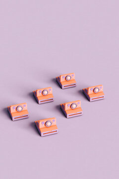 Three dimensional render of rows of instant cameras flat laid against purple background