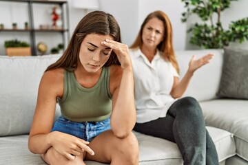 Mother and daughter unhappy arguing sitting on sofa at home