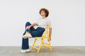 Middle-aged woman sitting on yellow chair and looking away isolated