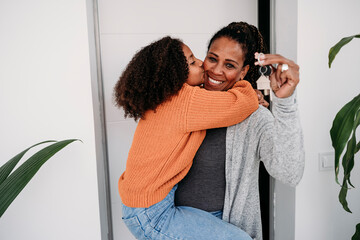 Happy girl embracing mother holding keys of new house