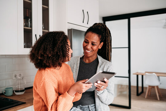 Happy mother and daughter with tablet PC in kitchen at home