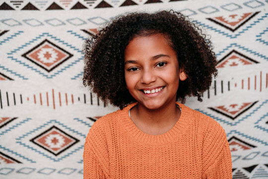 Happy Girl With Curly Hair In Front Of Patterned Backdrop