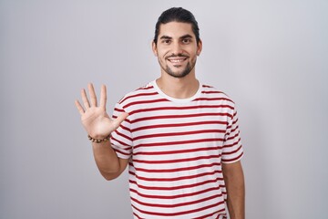 Fototapeta premium Hispanic man with long hair standing over isolated background showing and pointing up with fingers number five while smiling confident and happy.