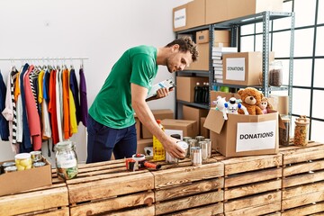 Young hispanic man wearing volunteer uniform holding canned food at charity center