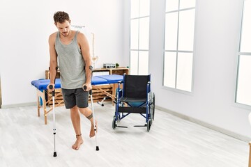 Fototapeta na wymiar Young hispanic man walking using crutches at clinic