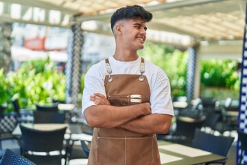 Young hispanic man waiter smiling confident standing with arms crossed gesture at coffee shop...