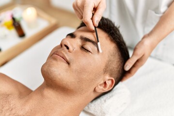 Young hispanic man relaxed having eyebrows treatment at beauty center