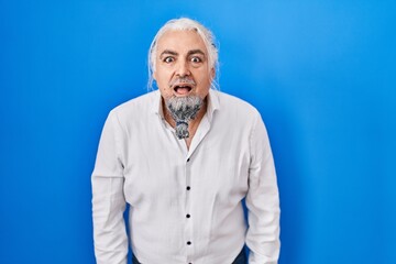 Middle age man with grey hair standing over blue background afraid and shocked with surprise and amazed expression, fear and excited face.