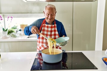 Senior man smiling confident cooking spaghetti at kitchen