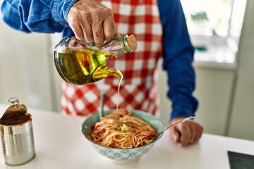 Senior man pouring oil on spaghetti at kitchen