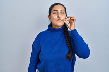 Young hispanic woman standing over isolated background mouth and lips shut as zip with fingers....