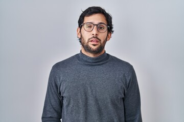 Handsome latin man standing over isolated background looking sleepy and tired, exhausted for fatigue and hangover, lazy eyes in the morning.