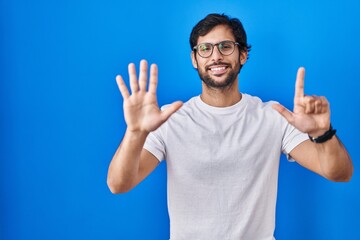 Handsome latin man standing over blue background showing and pointing up with fingers number seven while smiling confident and happy.