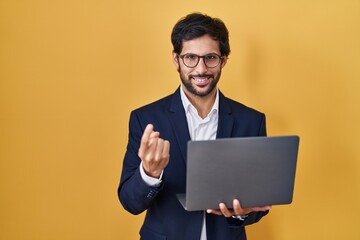 Handsome latin man working using computer laptop beckoning come here gesture with hand inviting welcoming happy and smiling