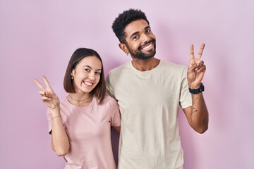 Young hispanic couple together over pink background smiling with happy face winking at the camera...