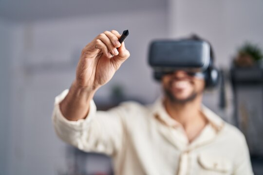 Young hispanic man artist using virtual reality glasses drawing at art studio