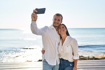 Man and woman couple hugging each other make selfie by the smartphone standing at seaside