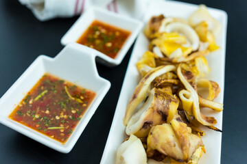 Grilled squid grilled over a charcoal grill eaten with seafood sauce, a popular street food in Thailand.