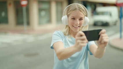 Young blonde woman smiling confident playing video game at street