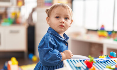 Adorable hispanic girl playing with construction blocks standing at kindergarten