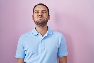 Obraz premium Hispanic man standing over pink background puffing cheeks with funny face. mouth inflated with air, crazy expression.
