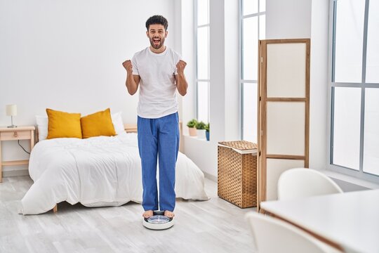 Arab man looking at weight machine to balance weight loss screaming proud, celebrating victory and success very excited with raised arms